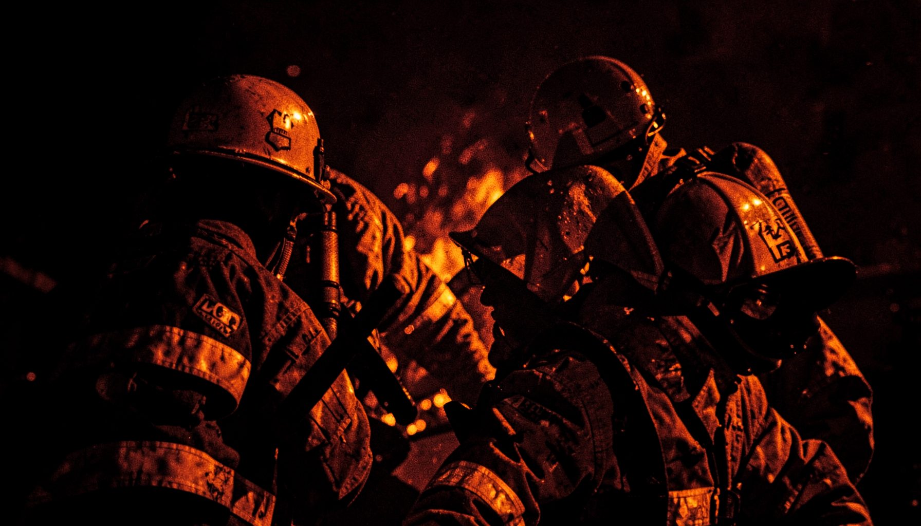 Firefighters in action with warm orange glow against dark background, intense mood