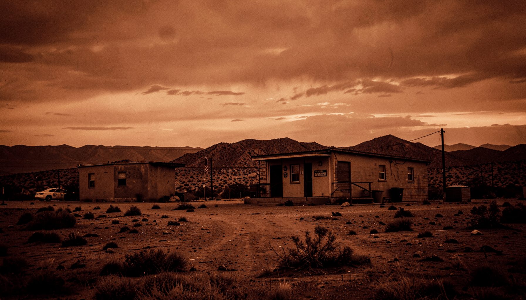 Desert landscape at dusk with a lone police station, warm amber and brown duotone, tense western mood